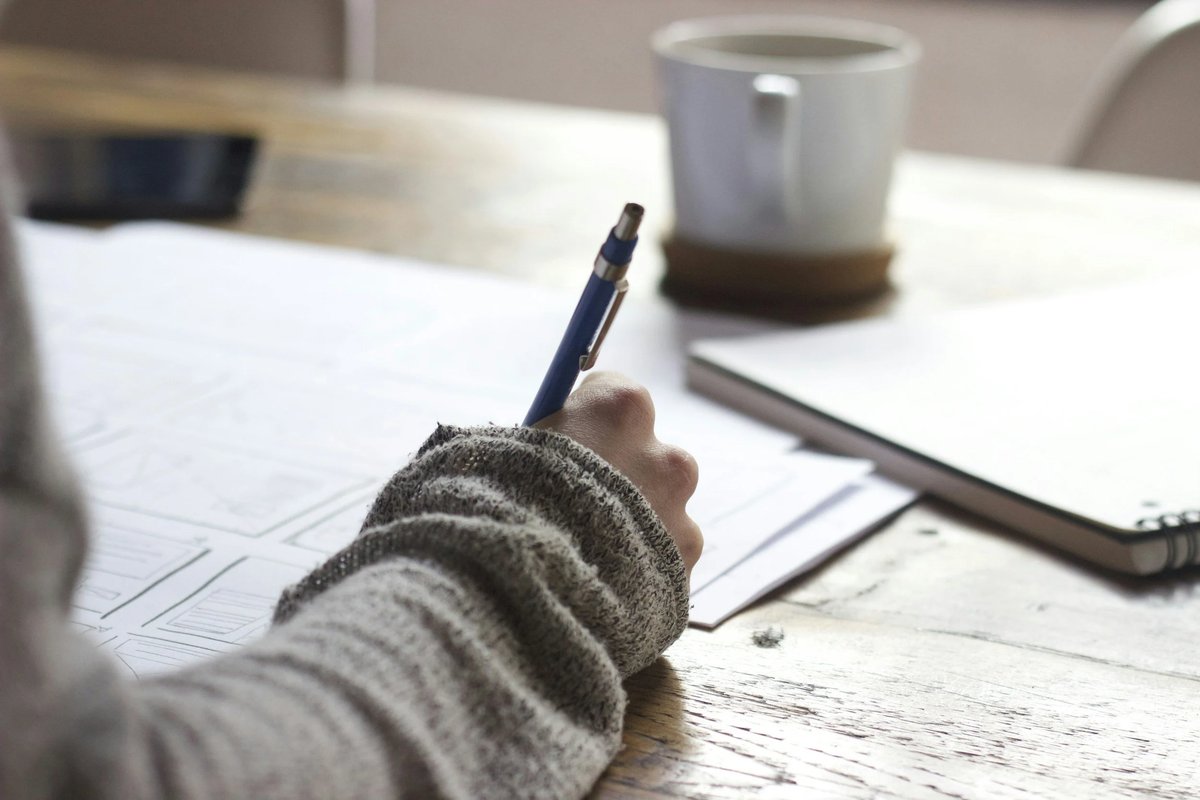 A student writing in a notebook with a cup of coffee, drafting a college essay