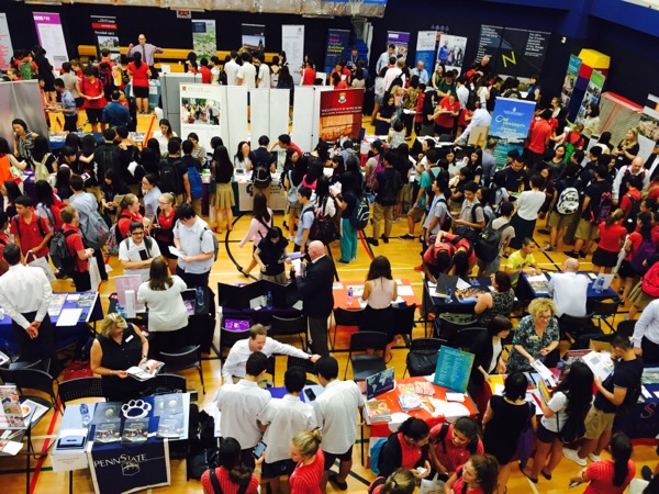 Students and parents at a fall college fair talking with admissions representatives on a busy gym floor